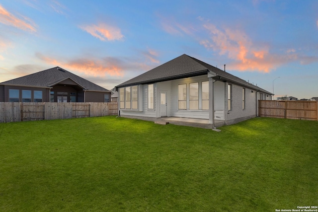 back house at dusk with a yard and a patio