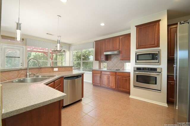 10606 Rainbow Vw, Helotes, TX 78023 - kitchen featuring backsplash, hanging light fixtures, a sink, under cabinet range hood, and stainless steel appliances
