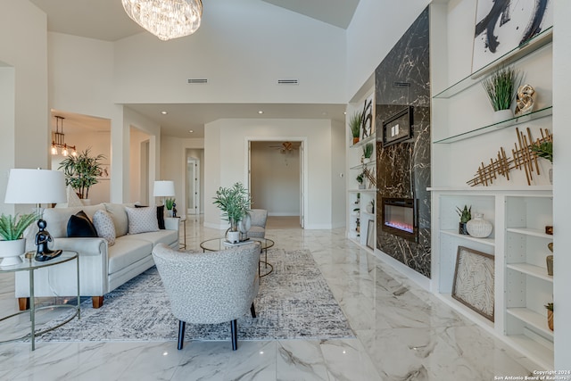 living room with built in shelves, a fireplace, a chandelier, and a high ceiling