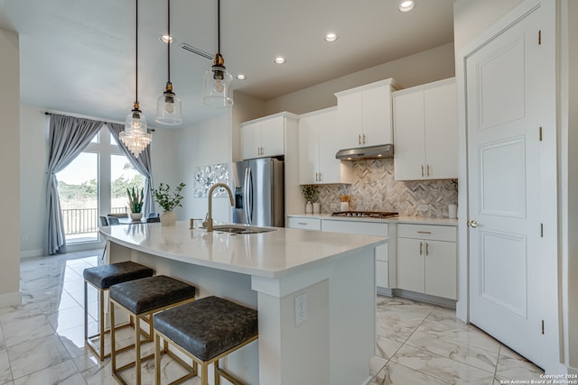 kitchen featuring a center island with sink, sink, appliances with stainless steel finishes, decorative light fixtures, and white cabinetry