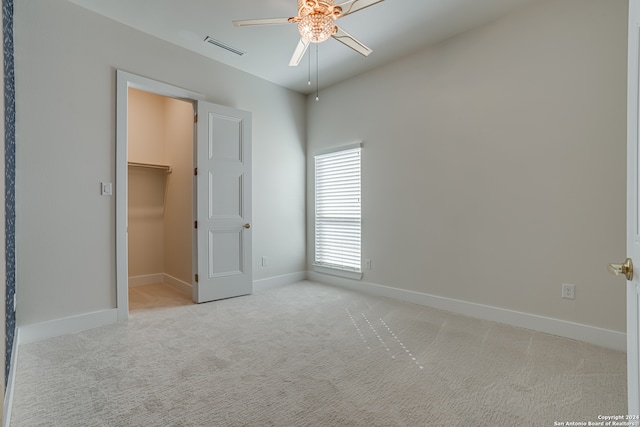 unfurnished bedroom with a walk in closet, ceiling fan, a closet, and light carpet