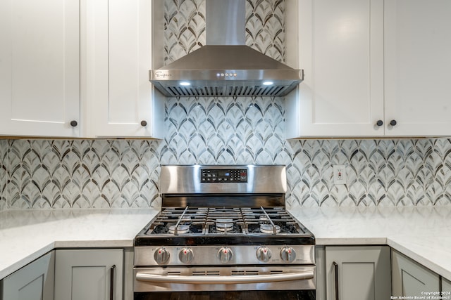 kitchen with gray cabinetry, stainless steel gas range oven, wall chimney exhaust hood, light stone countertops, and tasteful backsplash