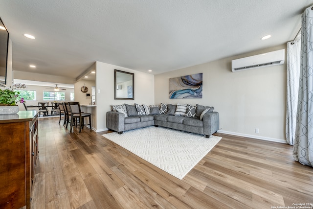 living room featuring a wall unit AC, a textured ceiling, and light wood-type flooring