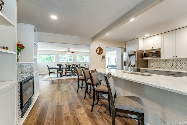 kitchen with a stone fireplace, tasteful backsplash, light stone counters, white cabinetry, and stainless steel appliances