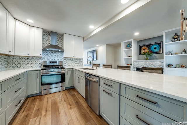 kitchen with sink, light hardwood / wood-style flooring, wall chimney exhaust hood, light stone countertops, and stainless steel appliances