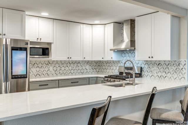 kitchen with white cabinetry, stainless steel appliances, wall chimney range hood, backsplash, and a breakfast bar