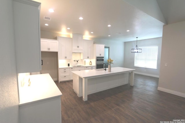 kitchen with decorative light fixtures, a center island with sink, dark wood-type flooring, white cabinetry, and stainless steel double oven