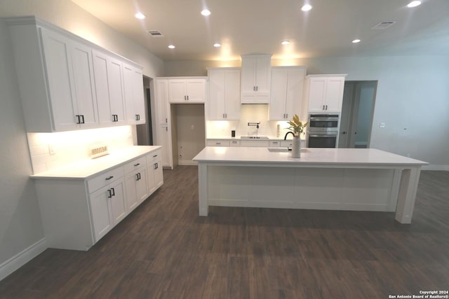 kitchen featuring stainless steel double oven, a center island with sink, white cabinetry, and dark hardwood / wood-style floors