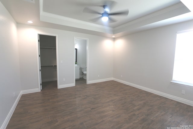 unfurnished bedroom featuring a raised ceiling, ceiling fan, a walk in closet, ensuite bathroom, and dark hardwood / wood-style floors