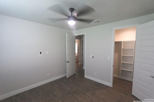 unfurnished bedroom with a spacious closet, ceiling fan, dark wood-type flooring, and a closet