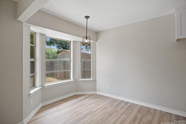 unfurnished dining area featuring an inviting chandelier, light hardwood / wood-style flooring, and plenty of natural light