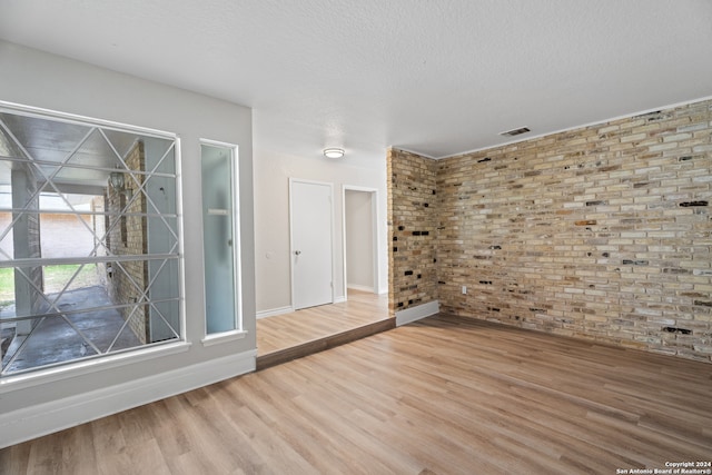 empty room featuring a textured ceiling, brick wall, and hardwood / wood-style floors