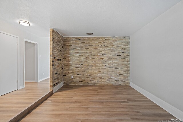 unfurnished room with a textured ceiling, light hardwood / wood-style flooring, and brick wall