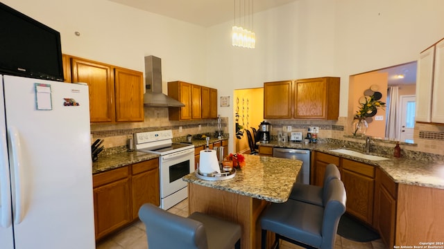 kitchen with white appliances, a high ceiling, a kitchen bar, sink, and wall chimney range hood