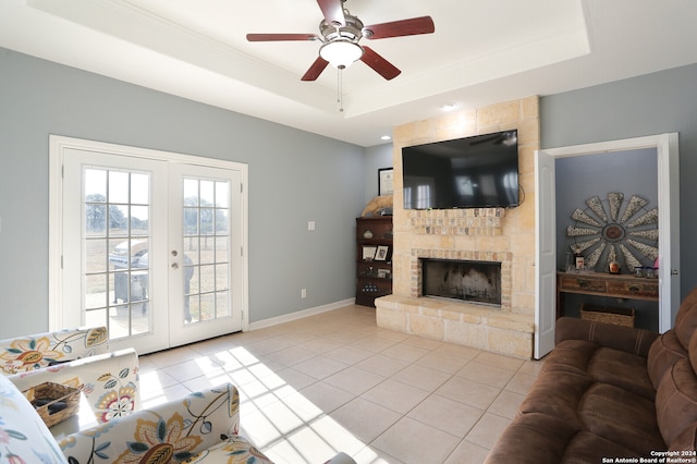 tiled living room with french doors, a tray ceiling, a fireplace, and ceiling fan