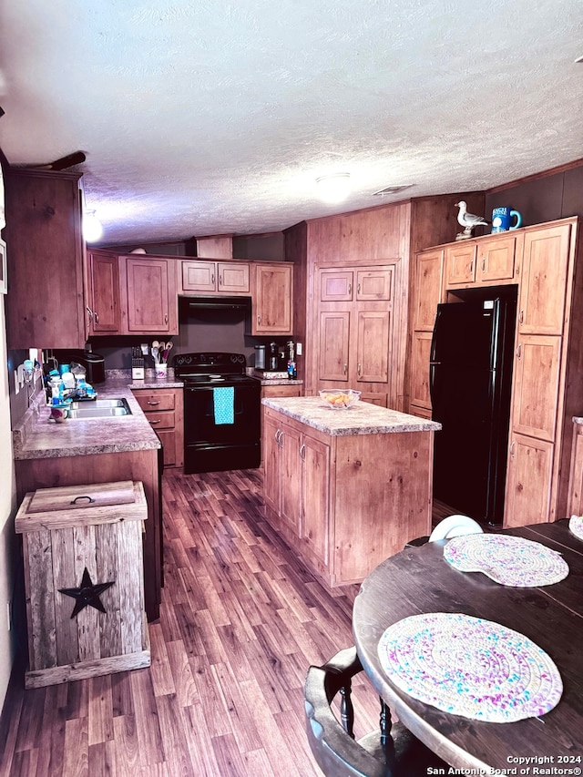 kitchen featuring a textured ceiling, a center island, hardwood / wood-style floors, and black appliances