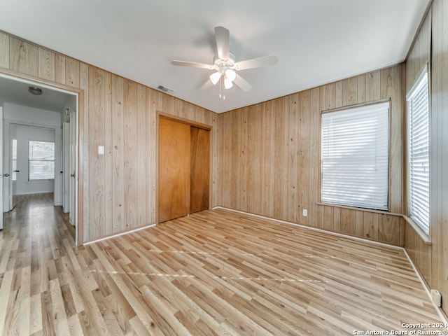 spare room featuring ceiling fan, light hardwood / wood-style flooring, and wood walls