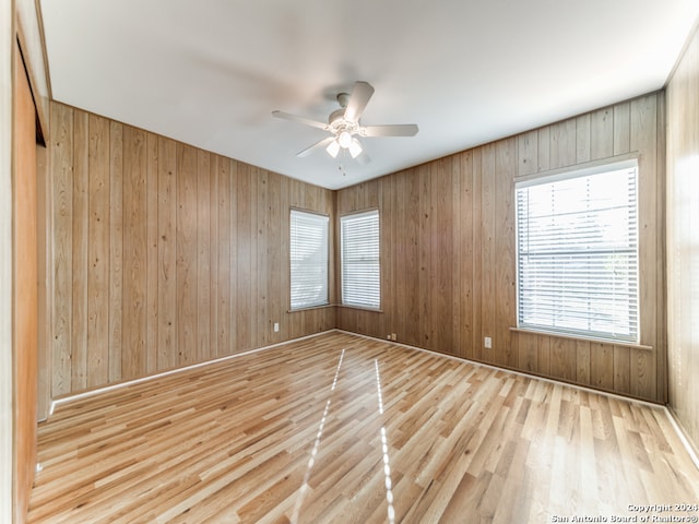 unfurnished room with wood walls, light hardwood / wood-style flooring, and ceiling fan