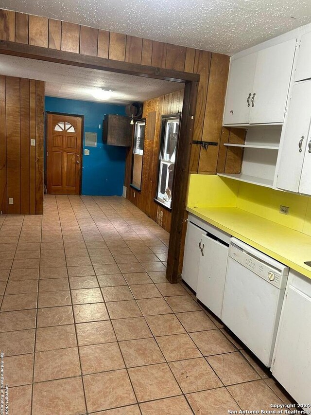 kitchen featuring white cabinets, dishwasher, wood walls, and a textured ceiling