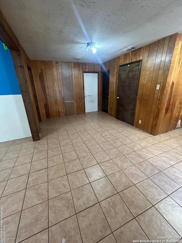 spare room featuring wooden walls, a textured ceiling, and light tile patterned floors