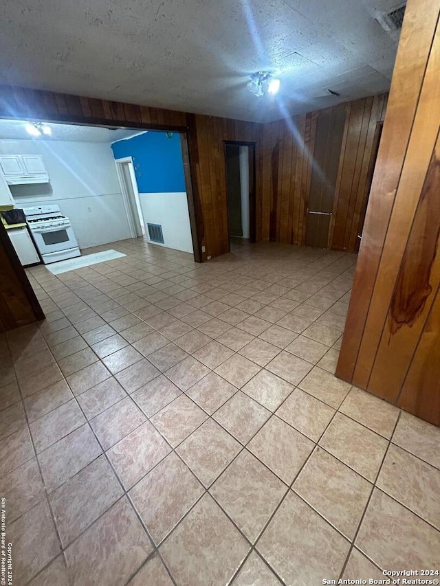 tiled empty room featuring a textured ceiling and wooden walls