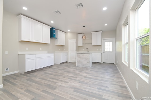 kitchen with pendant lighting, white cabinets, a kitchen island, wall chimney range hood, and light hardwood / wood-style floors