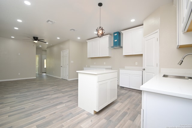 kitchen with white cabinets, light wood-type flooring, ceiling fan, sink, and wall chimney range hood