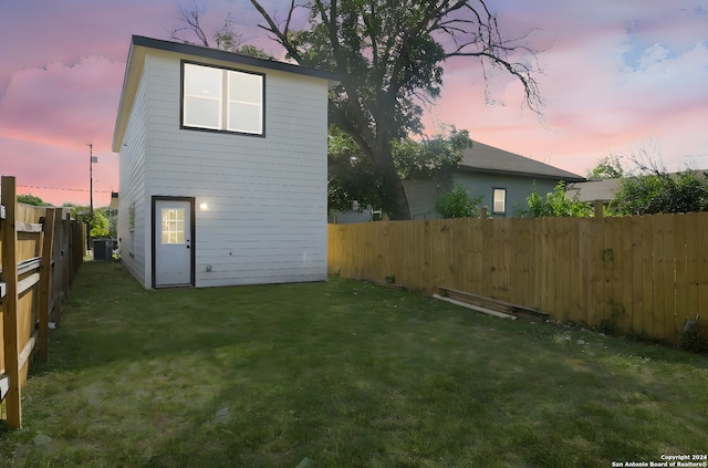 back house at dusk featuring a lawn and central air condition unit