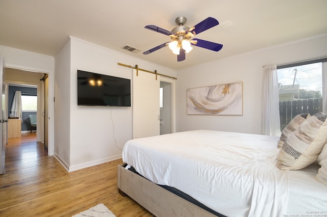 bedroom featuring ornamental molding, light wood-type flooring, ceiling fan, and a barn door