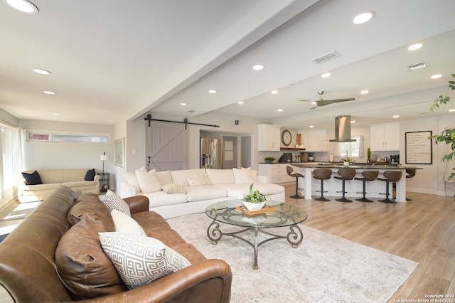 living room with light hardwood / wood-style flooring, beam ceiling, ceiling fan, and a barn door