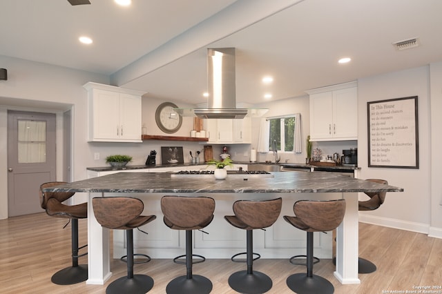 kitchen featuring white cabinets, island exhaust hood, dark stone counters, and light hardwood / wood-style floors