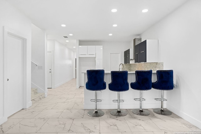 kitchen featuring decorative backsplash, kitchen peninsula, a breakfast bar area, and white cabinets