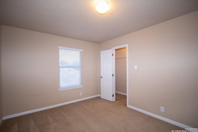 unfurnished bedroom featuring a spacious closet, a closet, and light carpet