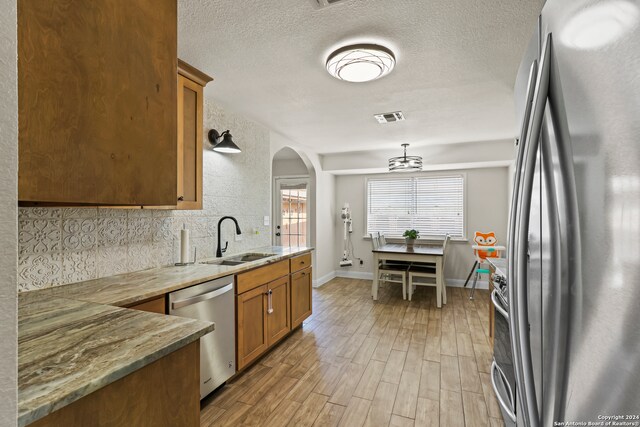 kitchen with appliances with stainless steel finishes, backsplash, a textured ceiling, light hardwood / wood-style flooring, and sink