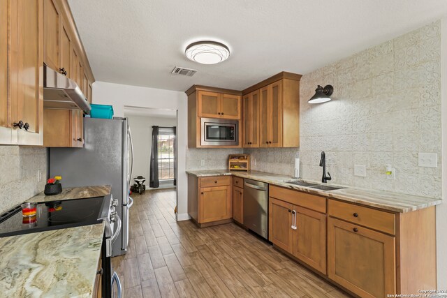 kitchen with light hardwood / wood-style floors, sink, backsplash, appliances with stainless steel finishes, and light stone countertops