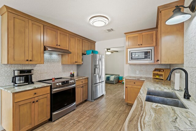 kitchen with light stone counters, light hardwood / wood-style floors, sink, appliances with stainless steel finishes, and ceiling fan