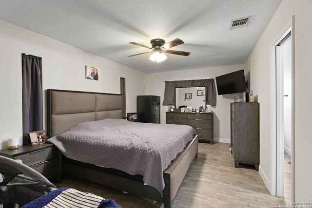 bedroom with a textured ceiling, light hardwood / wood-style floors, and ceiling fan