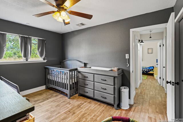 bedroom featuring light hardwood / wood-style floors, a crib, and ceiling fan