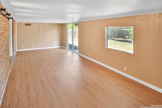 empty room with ornamental molding, wooden walls, light wood-type flooring, and a barn door