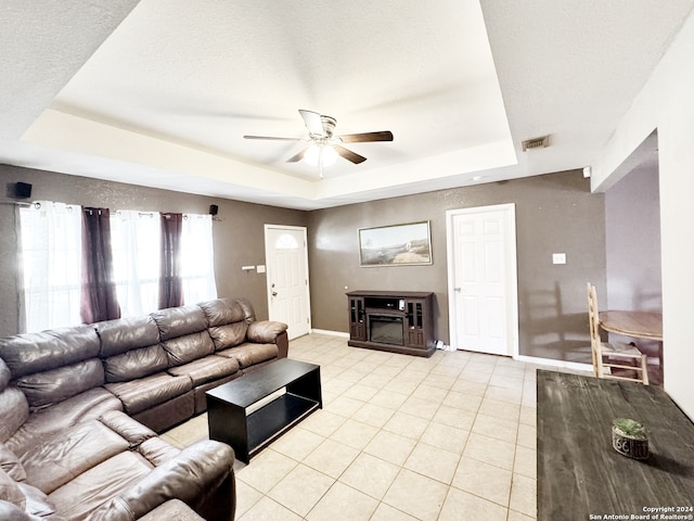 tiled living room with a textured ceiling, a raised ceiling, a fireplace, and ceiling fan