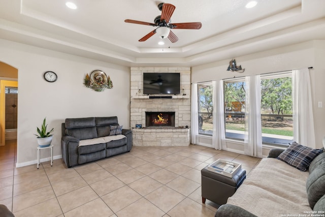 tiled living room with ceiling fan, a fireplace, and a tray ceiling