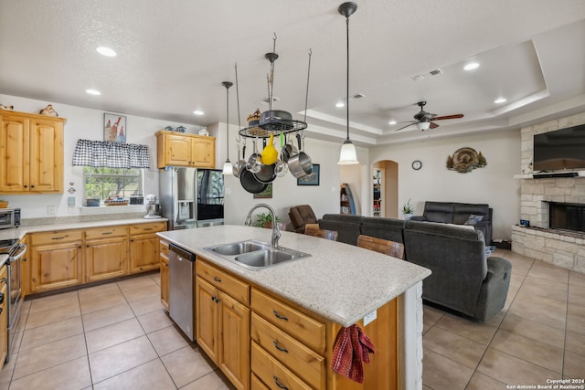 kitchen featuring a stone fireplace, stainless steel appliances, ceiling fan, a kitchen island with sink, and sink