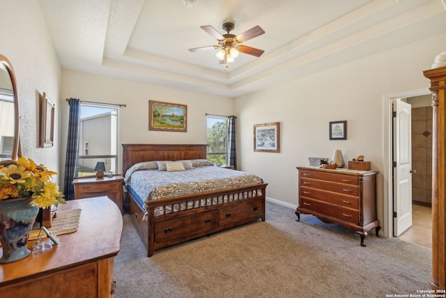 bedroom featuring carpet flooring, a tray ceiling, ensuite bath, and ceiling fan