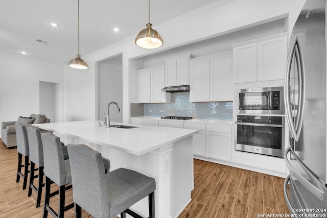 kitchen featuring hanging light fixtures, light hardwood / wood-style floors, an island with sink, white cabinets, and stainless steel appliances