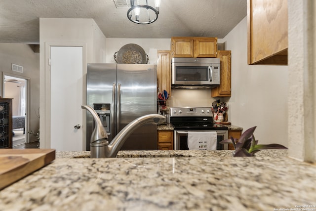 kitchen featuring appliances with stainless steel finishes, a textured ceiling, and light stone countertops