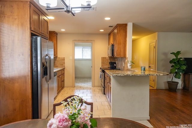 kitchen featuring a breakfast bar, light wood-type flooring, tasteful backsplash, appliances with stainless steel finishes, and light stone countertops