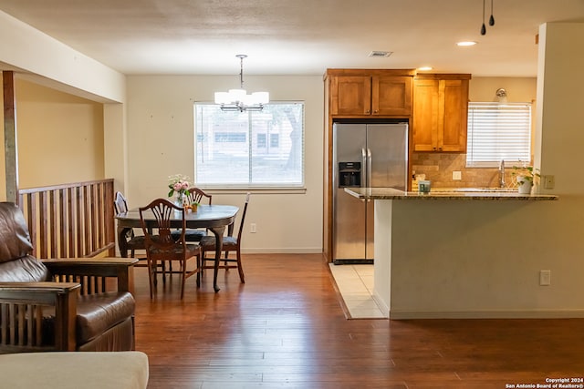 kitchen featuring hanging light fixtures, stainless steel refrigerator with ice dispenser, a notable chandelier, dark stone counters, and hardwood / wood-style floors