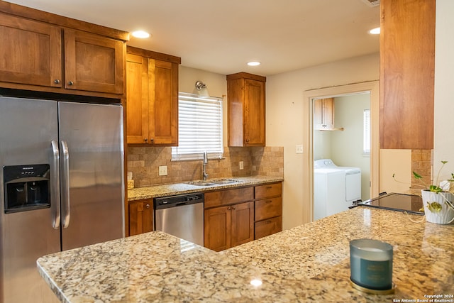 kitchen with appliances with stainless steel finishes, light stone counters, backsplash, sink, and washing machine and clothes dryer