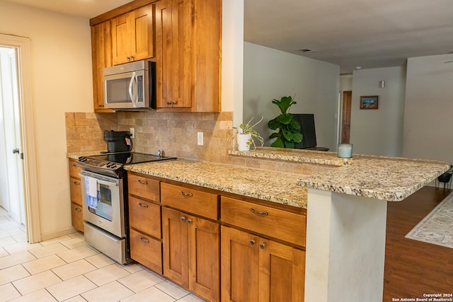 kitchen featuring light wood-type flooring, tasteful backsplash, kitchen peninsula, appliances with stainless steel finishes, and light stone countertops