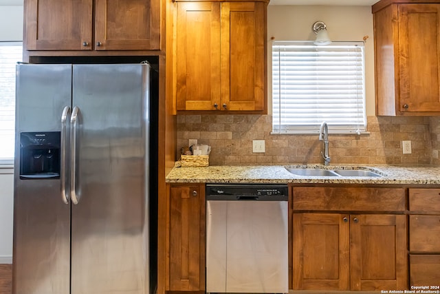 kitchen featuring light stone countertops, backsplash, sink, and stainless steel appliances